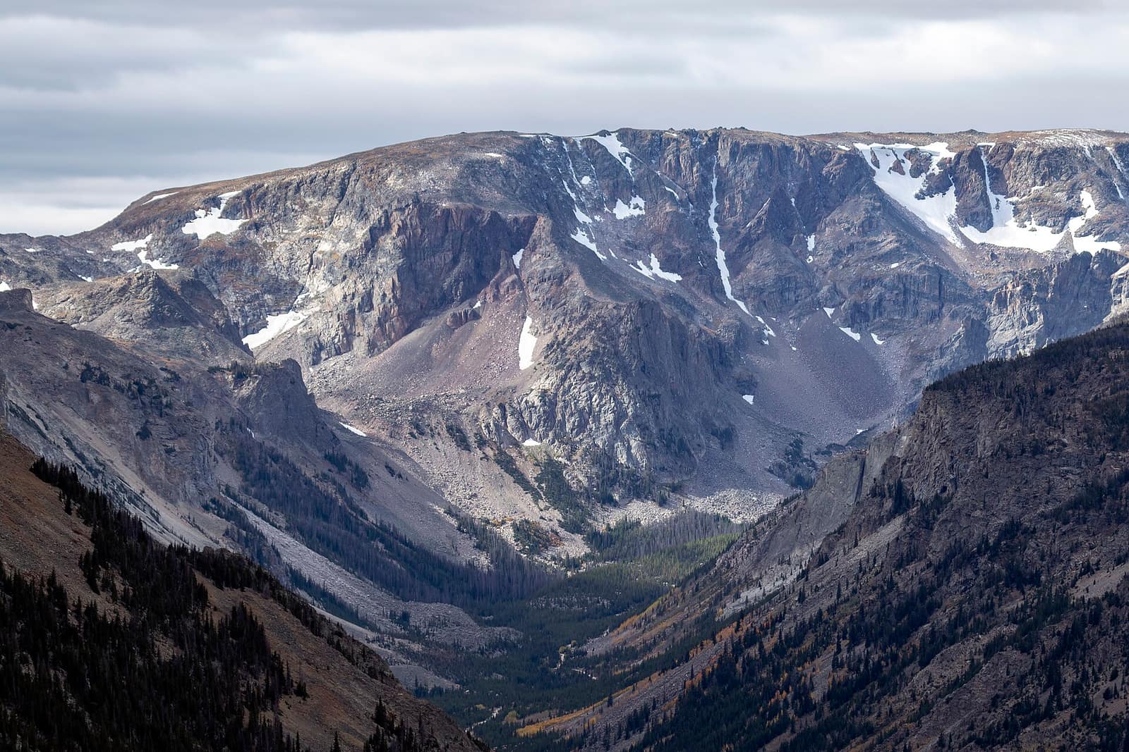 Rugged rocky peaks and the deep Rock Creek Valley seen from the Beartooth Highway in Montana, with snow patches on the upper cliffs