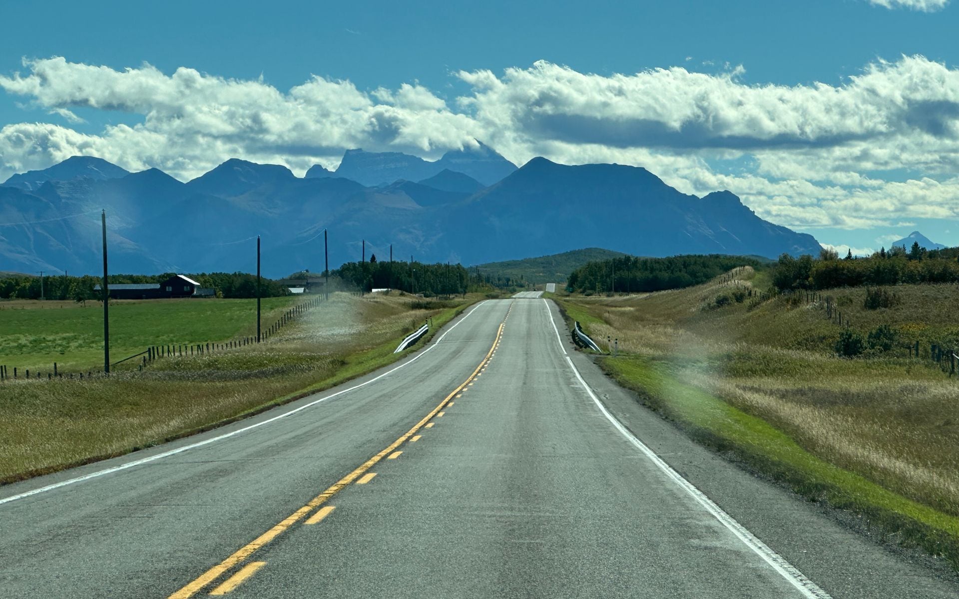 A car parked at a pullout on a wide Montana highway with the Rocky Mountain Front visible in the distance